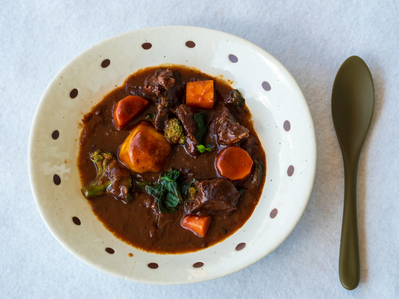 Un bol de ragoût de bœuf avec des pommes de terre et des carottes servi dans un plat de couleur crème