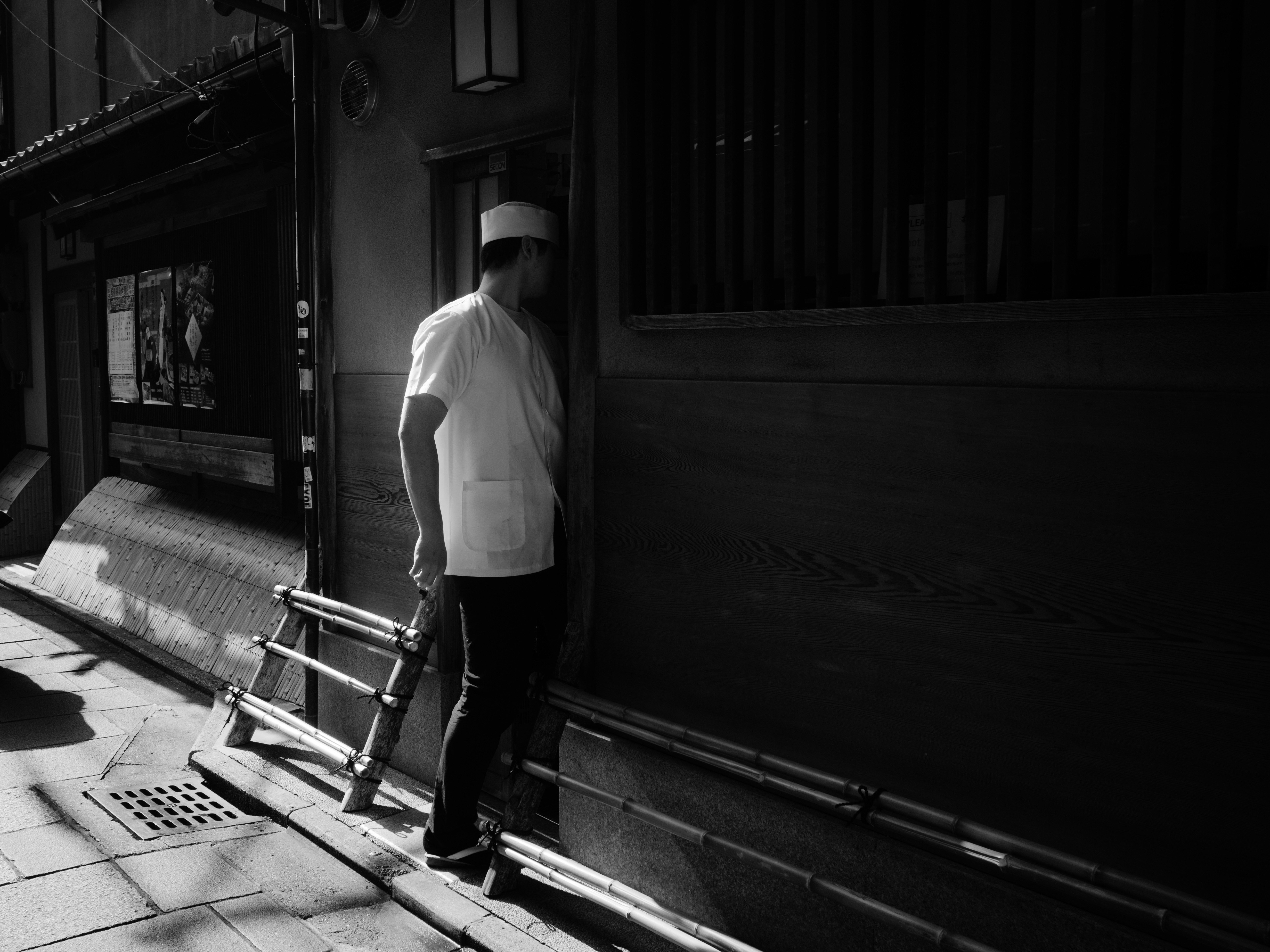 instantánea en blanco y negro de una persona de pie junto a una escalera en un callejón