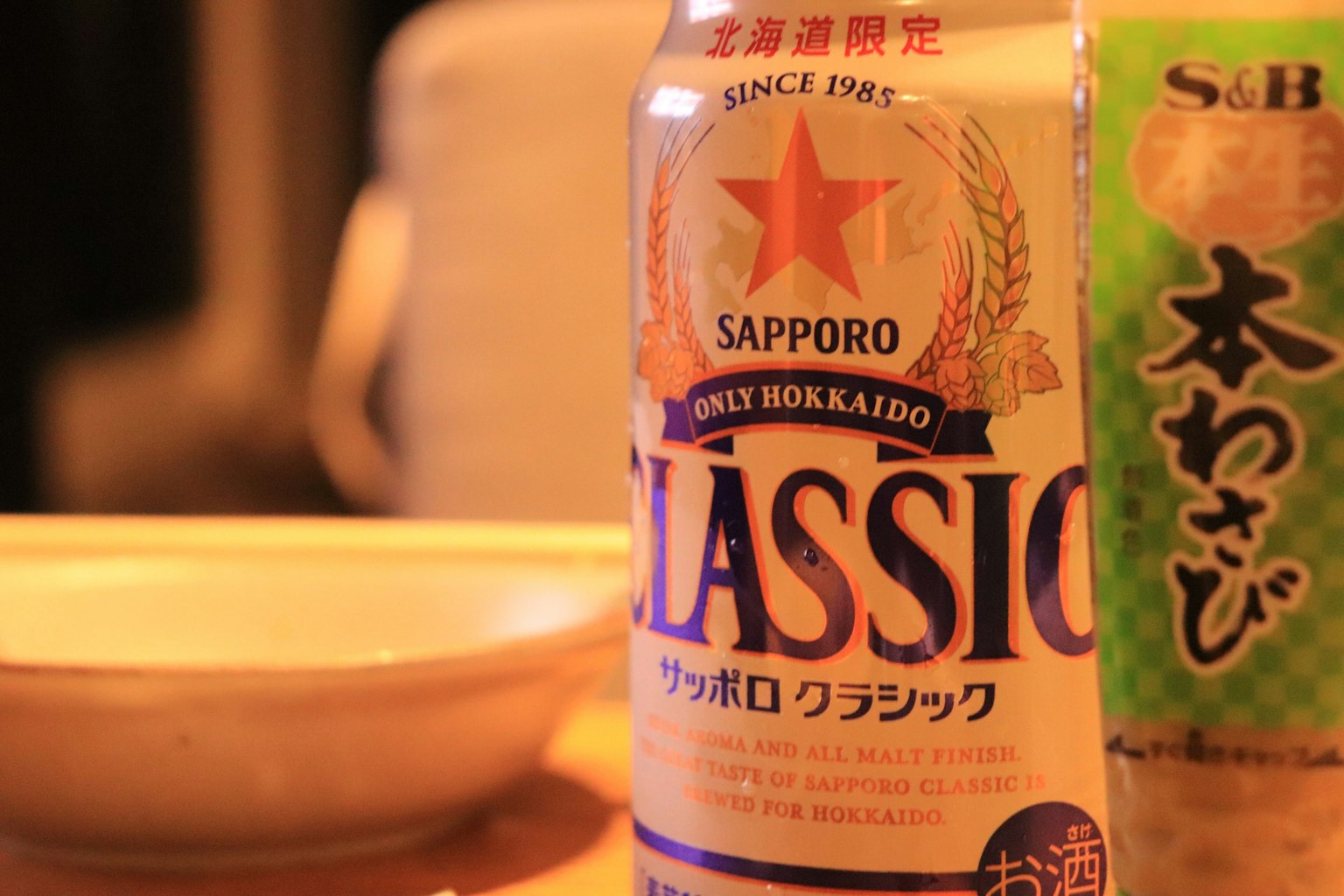 Lattina di birra Sapporo Classic accanto a una bottiglia di wasabi su un tavolo