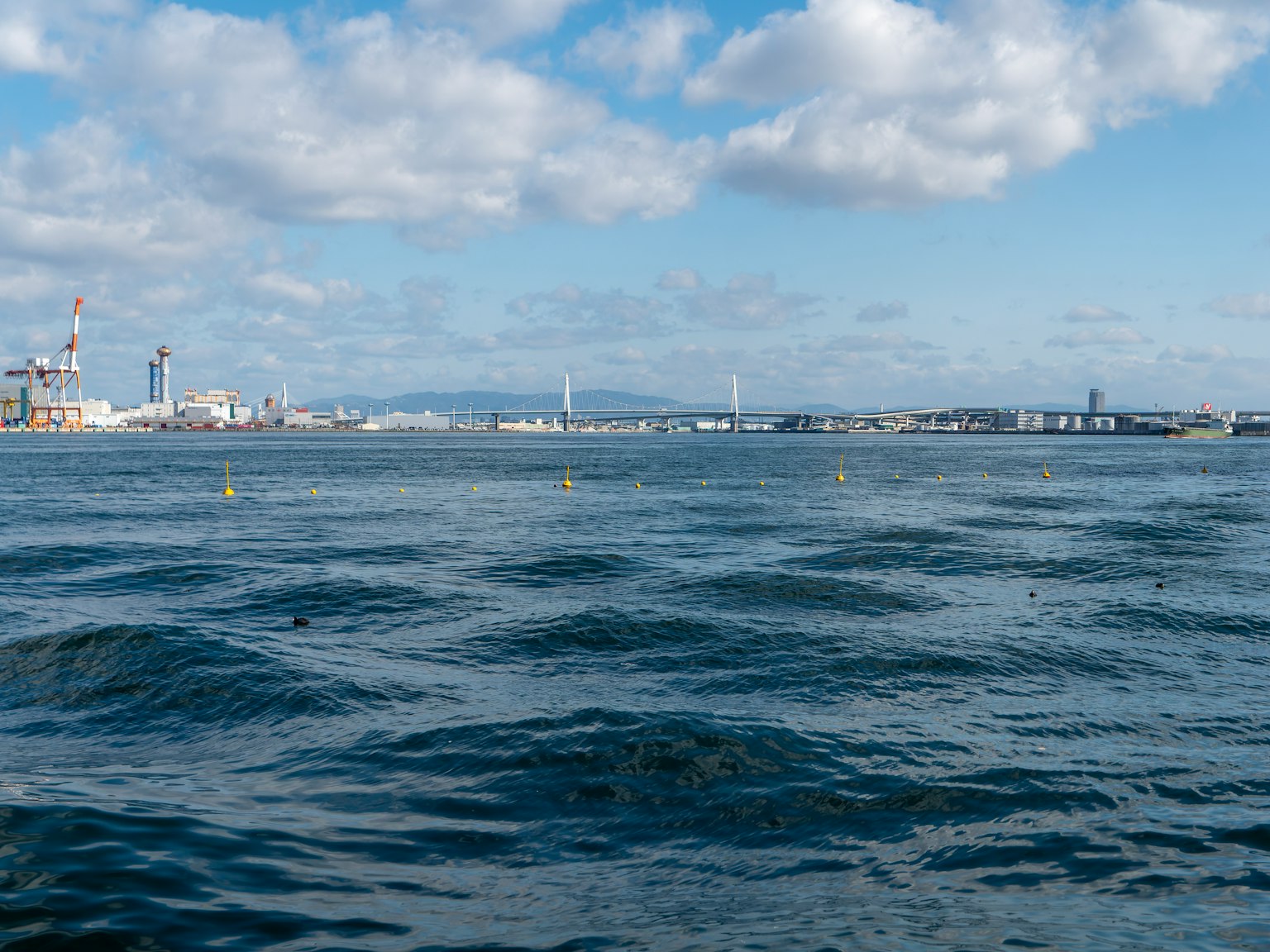 藍色海洋與柔和波浪及建築物與起重機的天際線