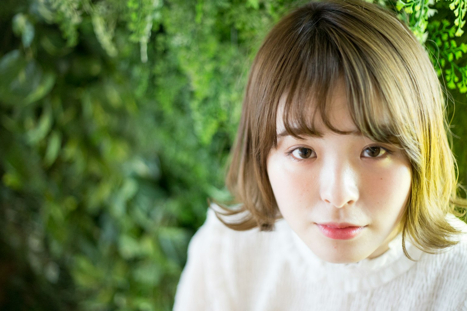 녹색 배경 앞에 서 있는 젊은 여성의 초상 밝은 색 스웨터 착용