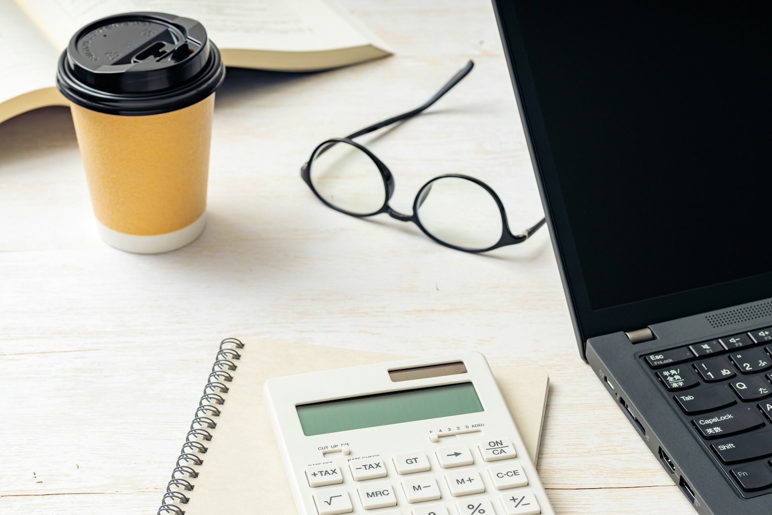 Ein einfacher Arbeitsplatz mit Laptop, Taschenrechner, Kaffeetasse und Brille auf einem Tisch