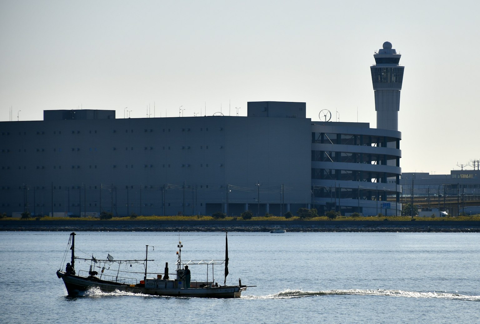 Bateau de pêche naviguant sur l'eau avec une tour d'aéroport en arrière-plan