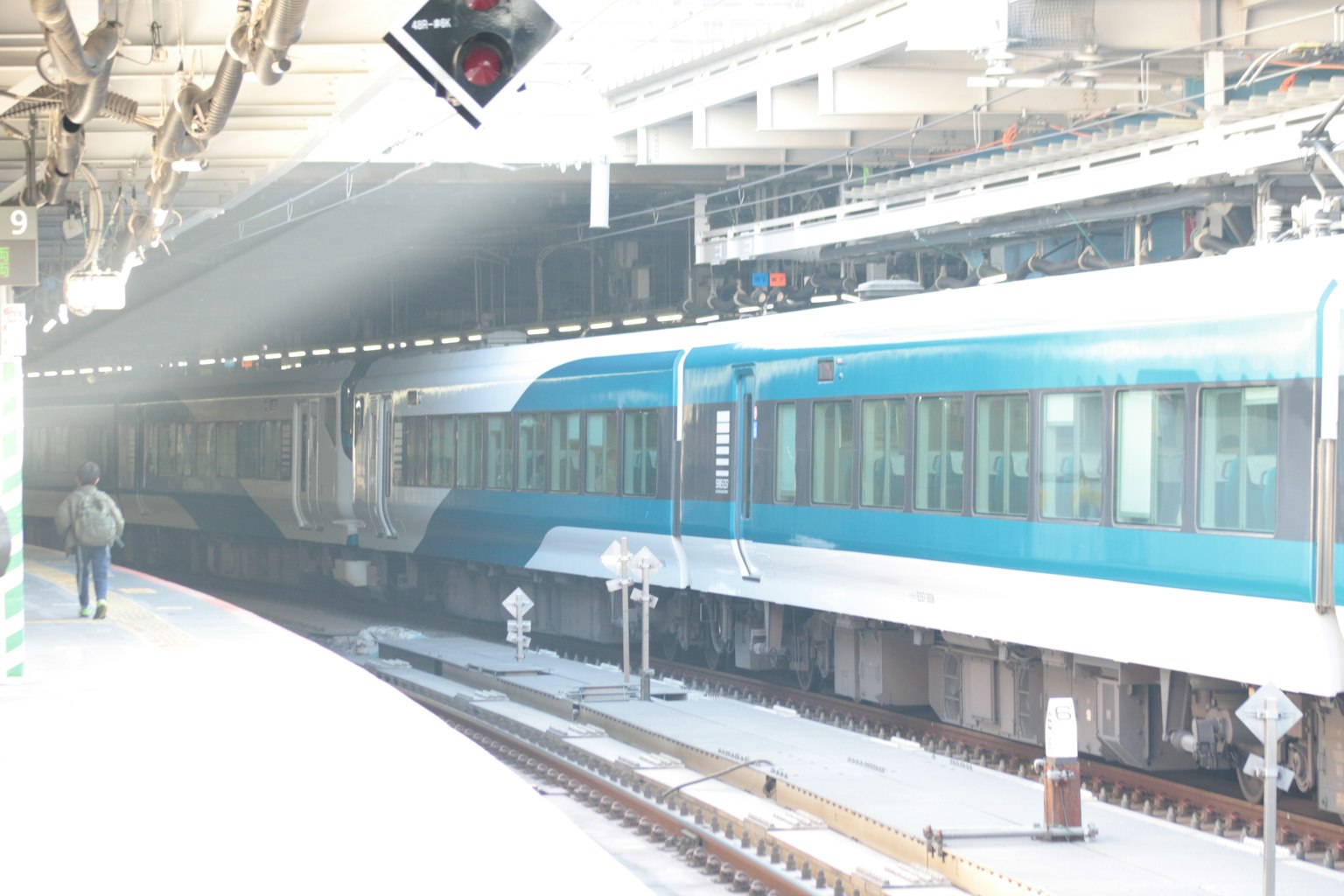Un train bleu sur un quai de gare avec un feu de signalisation au-dessus