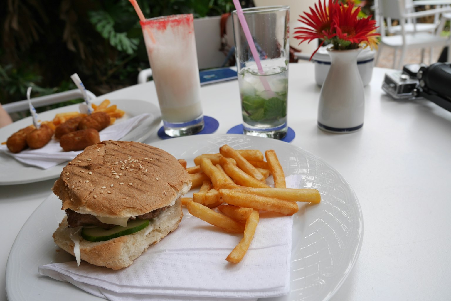 Une assiette avec un hamburger et des frites sur une table avec des boissons et des fleurs en arrière-plan