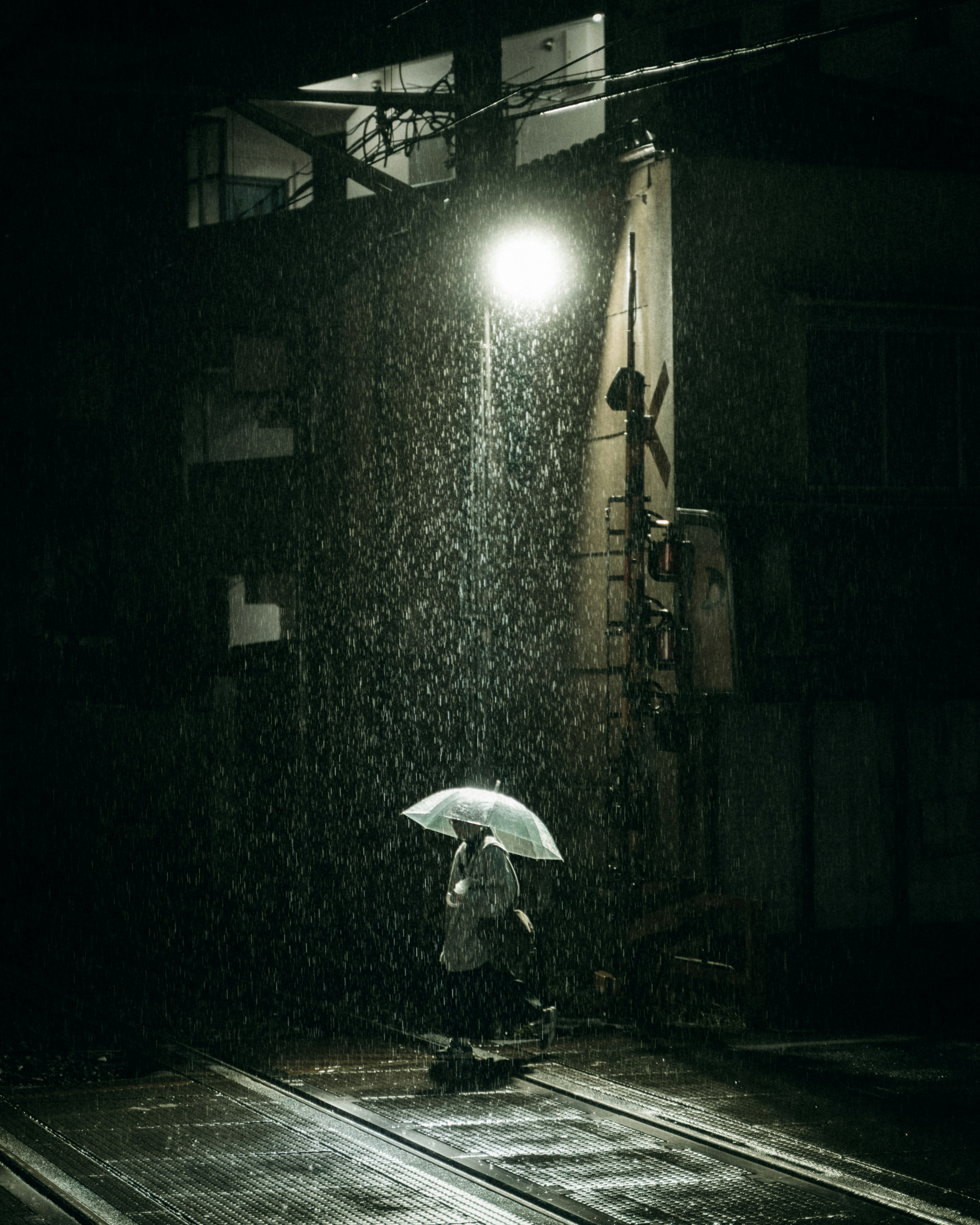 雨の駅前で傘をさす人のいる路地
