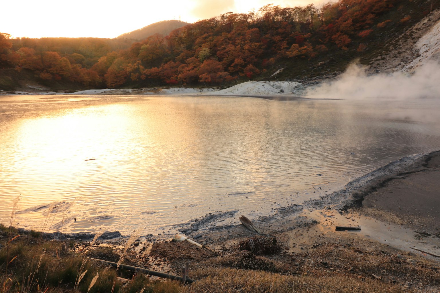 Scenic view of a hot spring with a calm water surface and autumn foliage during sunset