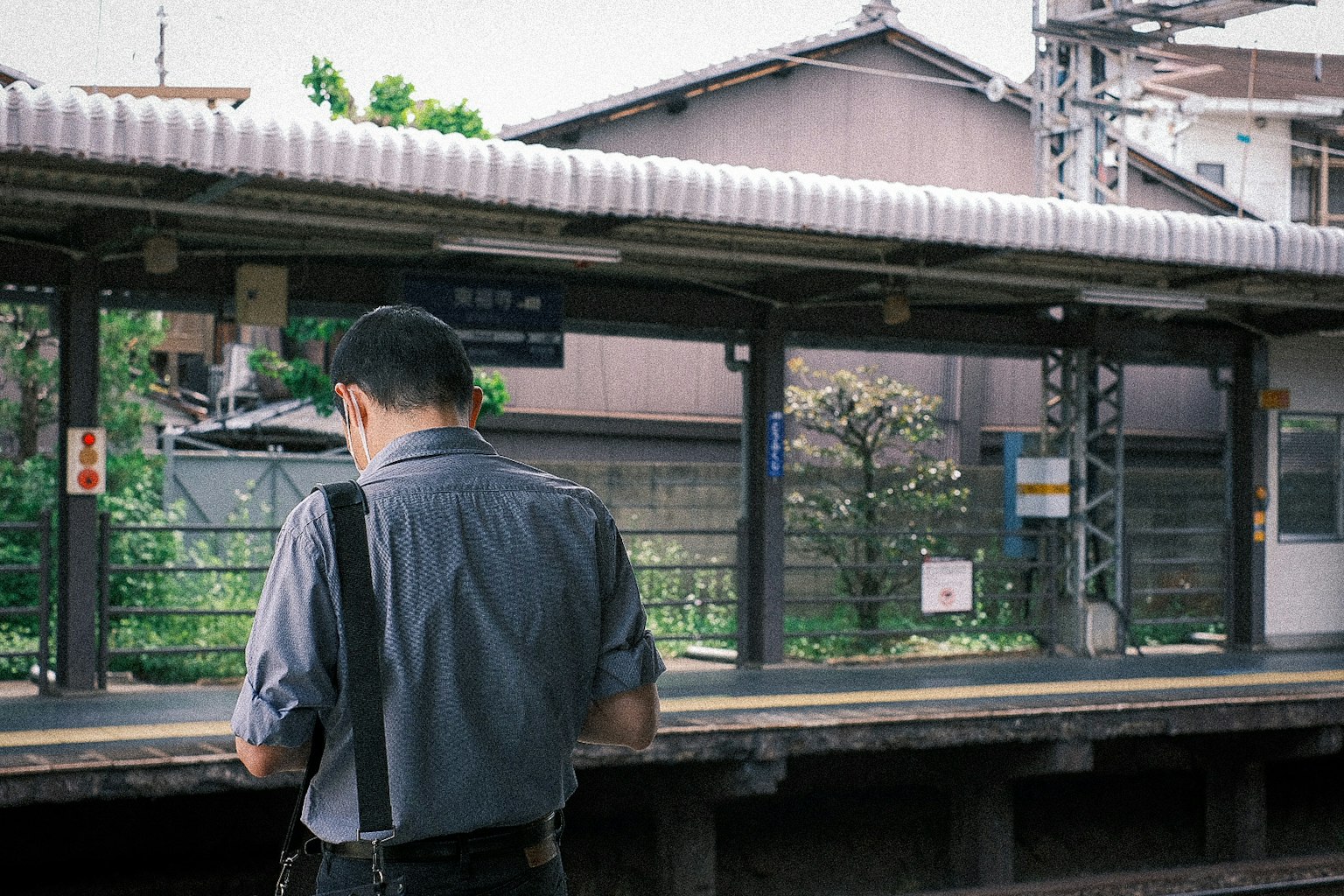 Man standing on train platform with a view of the station and surrounding greenery