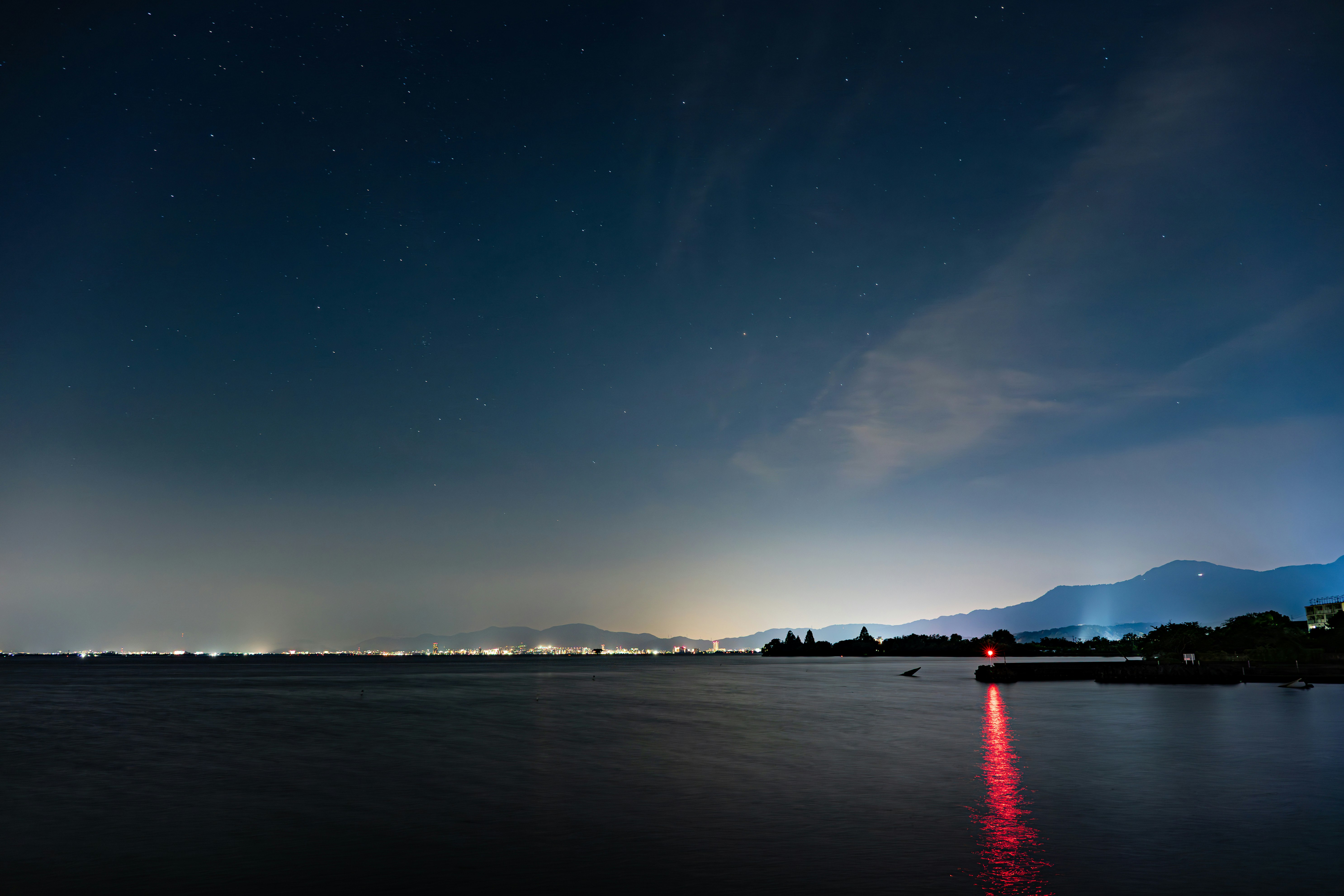 夜の湖畔に伸びる赤い光の反射と星空