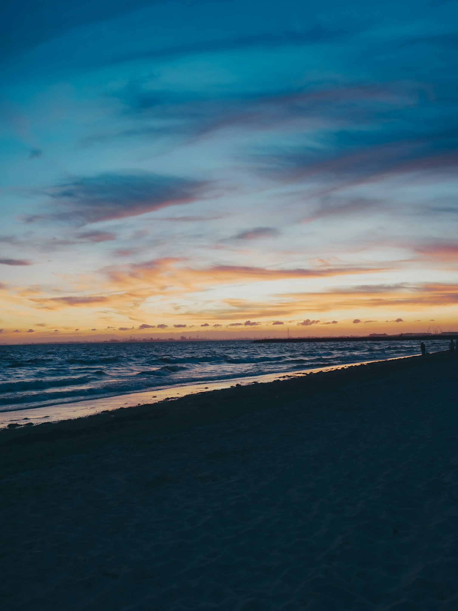Vista panoramica di una spiaggia al tramonto con nuvole colorate e onde leggere