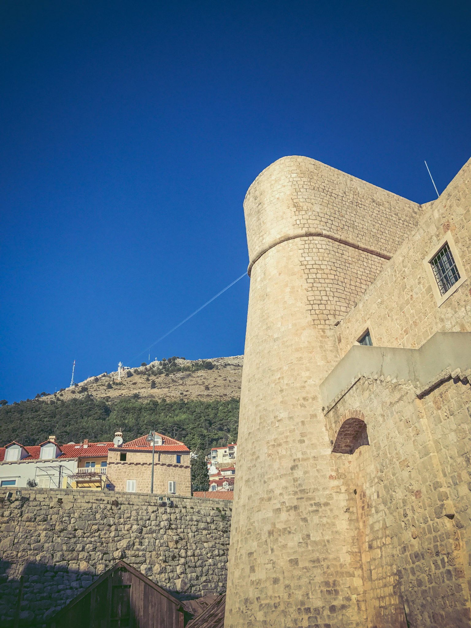 Antico muro di pietra sotto un cielo blu con edifici circostanti
