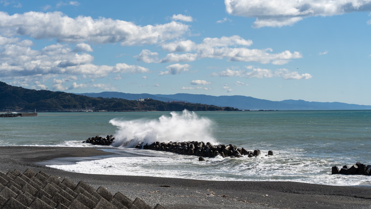 Scène côtière avec mer bleue et vagues s'écrasant montagnes et nuages en arrière-plan