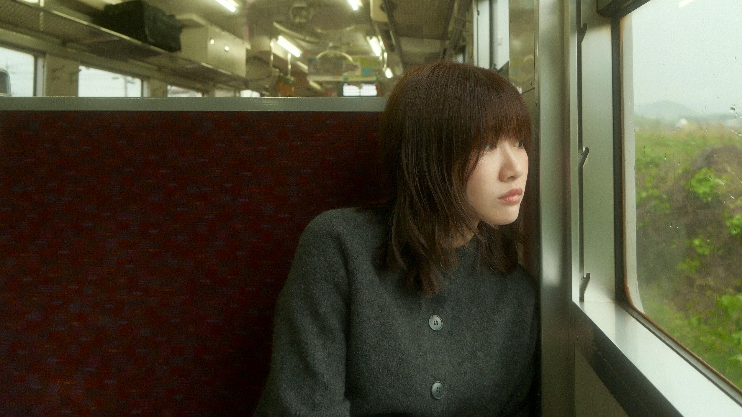 雨の窓辺で電車内の席に座る一人の女性