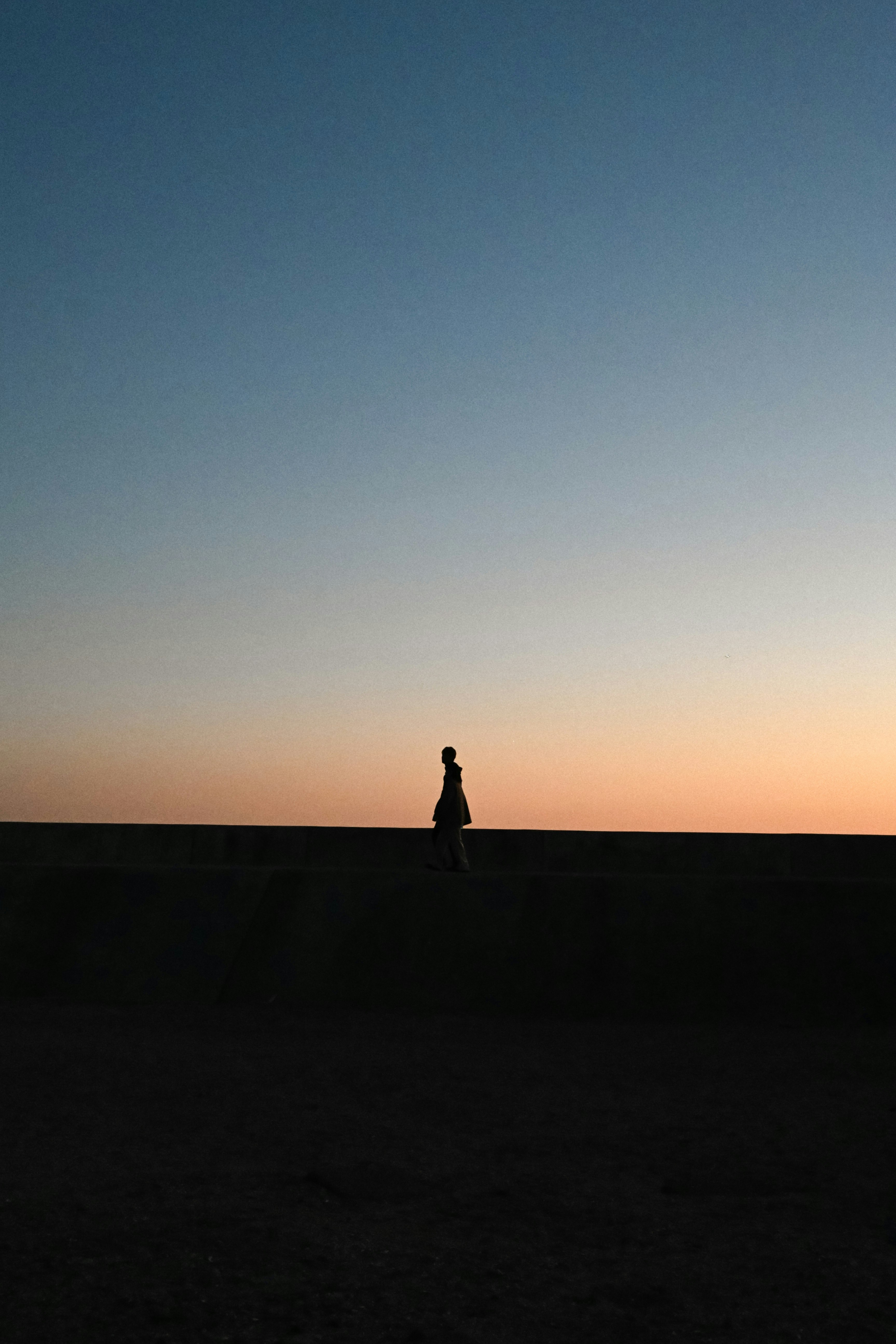 夕焼けの空と海辺の防波堤に立つ人物
