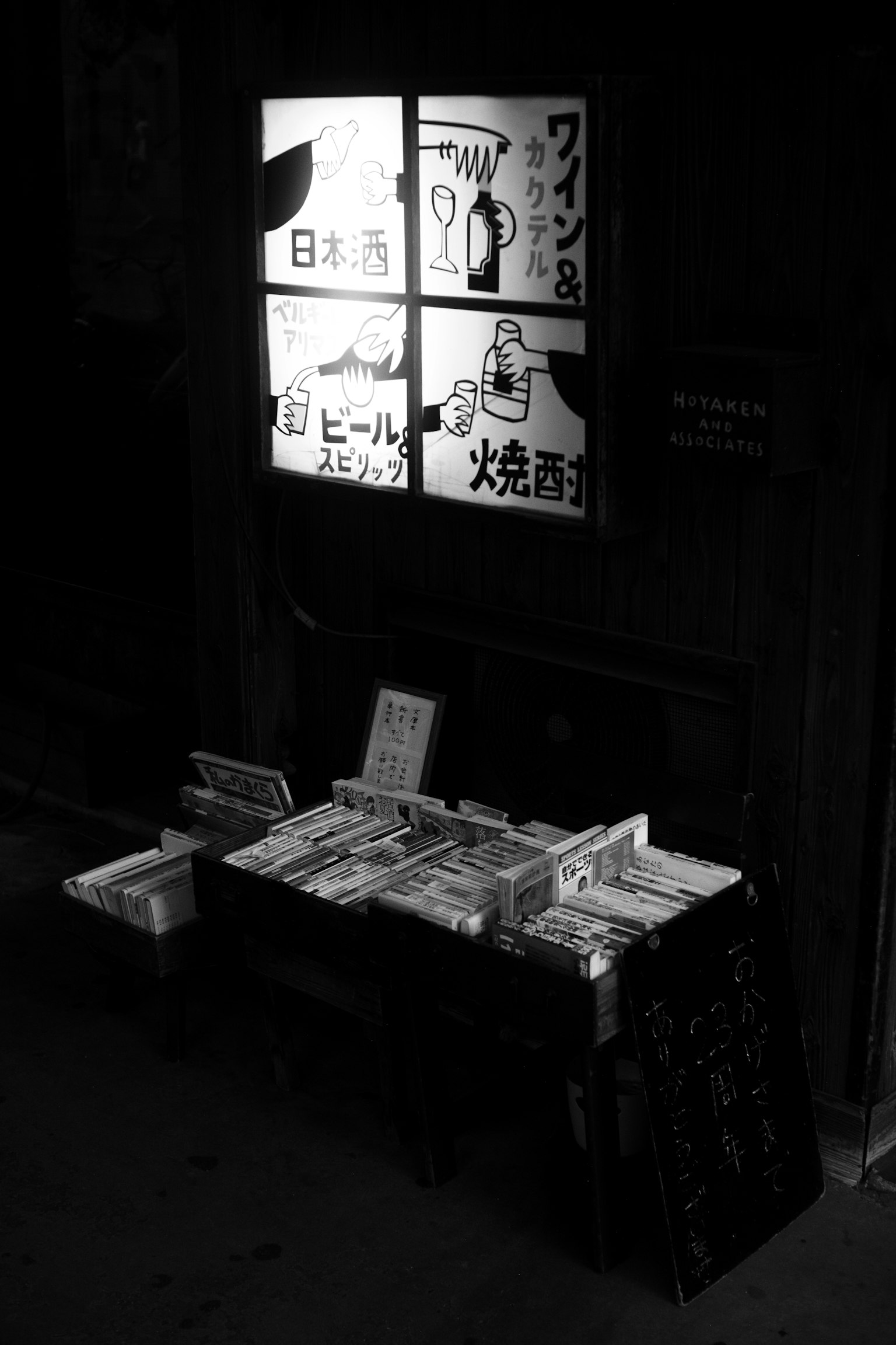 A dimly lit scene featuring a table with books and menus under a illuminated window with Japanese signs