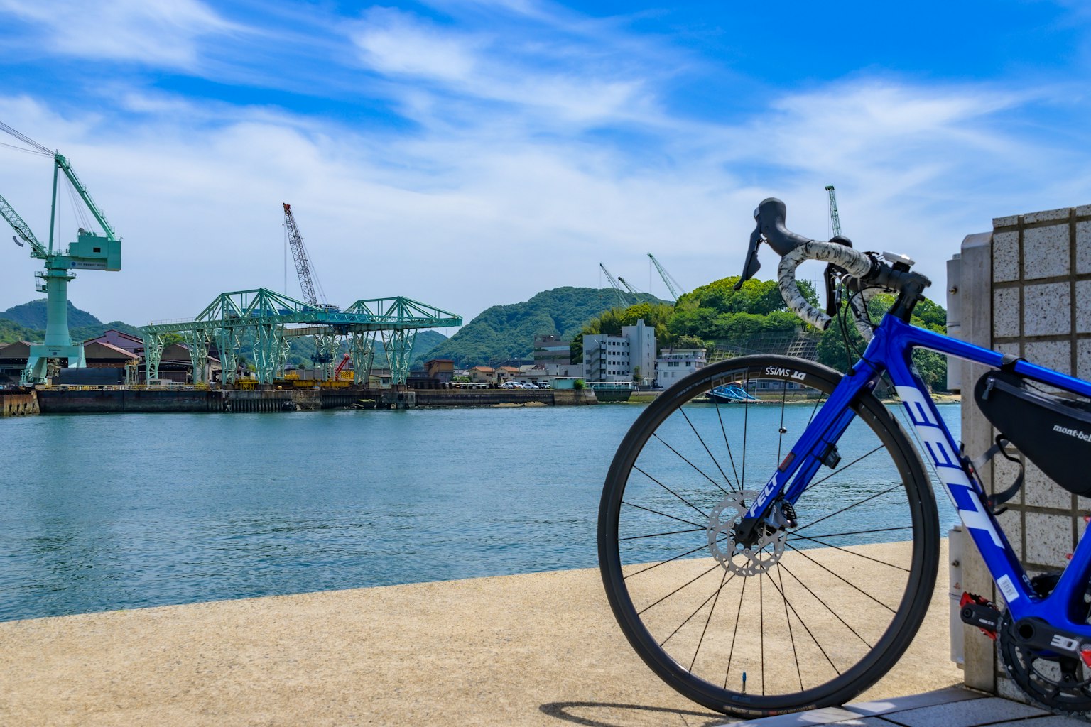 Una bicicletta blu posizionata vicino al porto con gru e uno sfondo panoramico