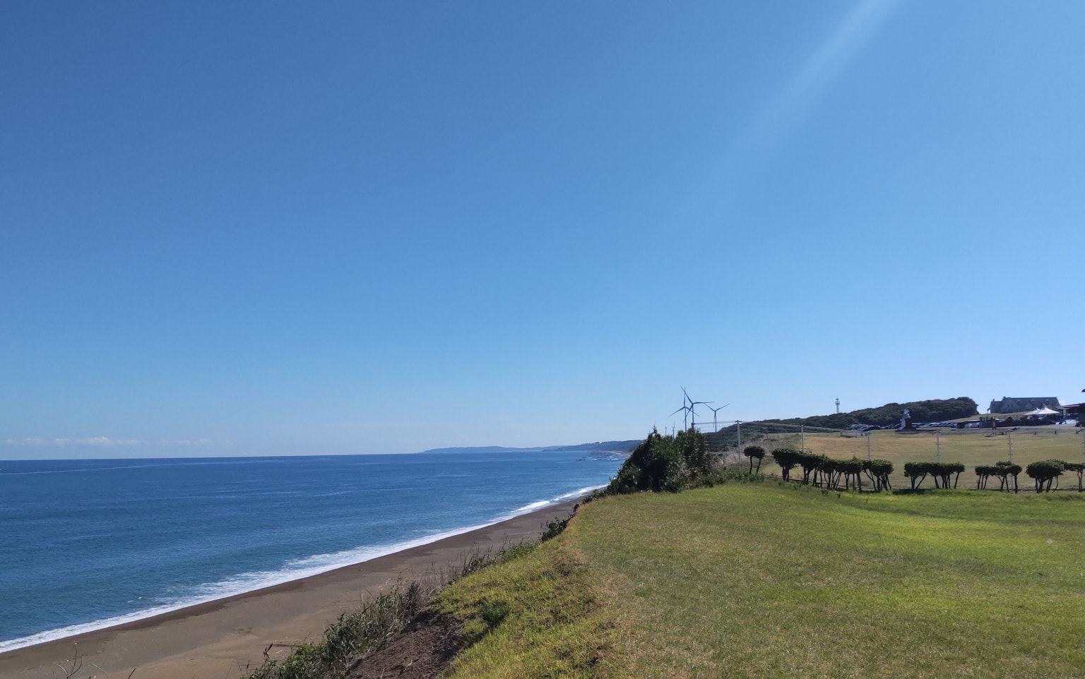 Scenic view of blue ocean and clear sky green meadow and distant houses