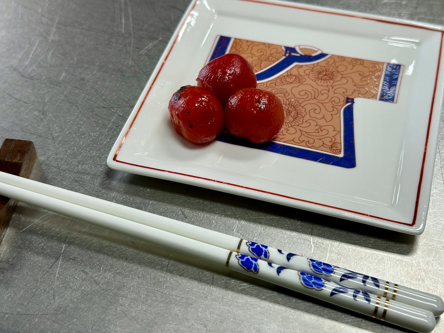 Un piatto bianco con tre pomodori rossi e le bacchette accanto