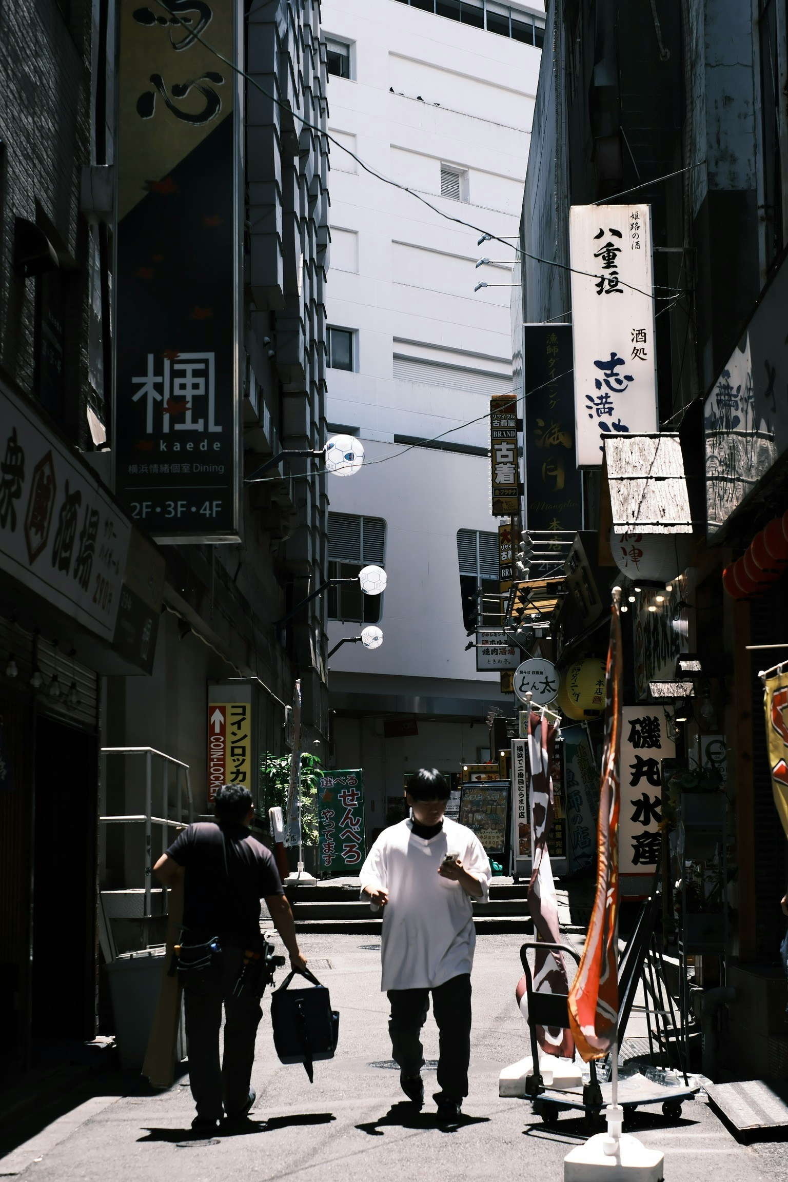Two men walking in a narrow alley with surrounding signs