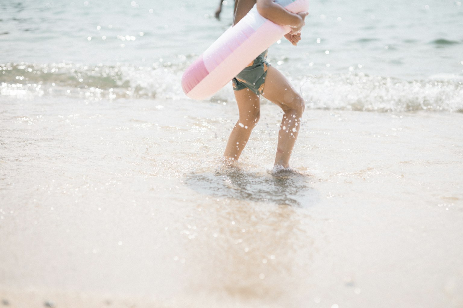 Niño jugando en la playa sosteniendo un flotador rosa