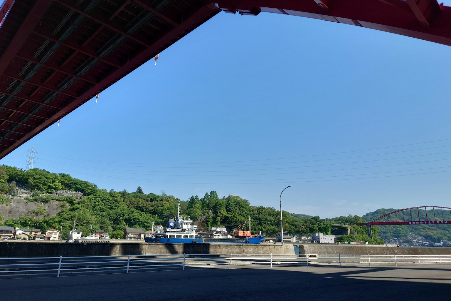 ทิวทัศน์ของท่าเรือใต้สะพานแดงที่มีเรือและเนินเขาสีเขียว