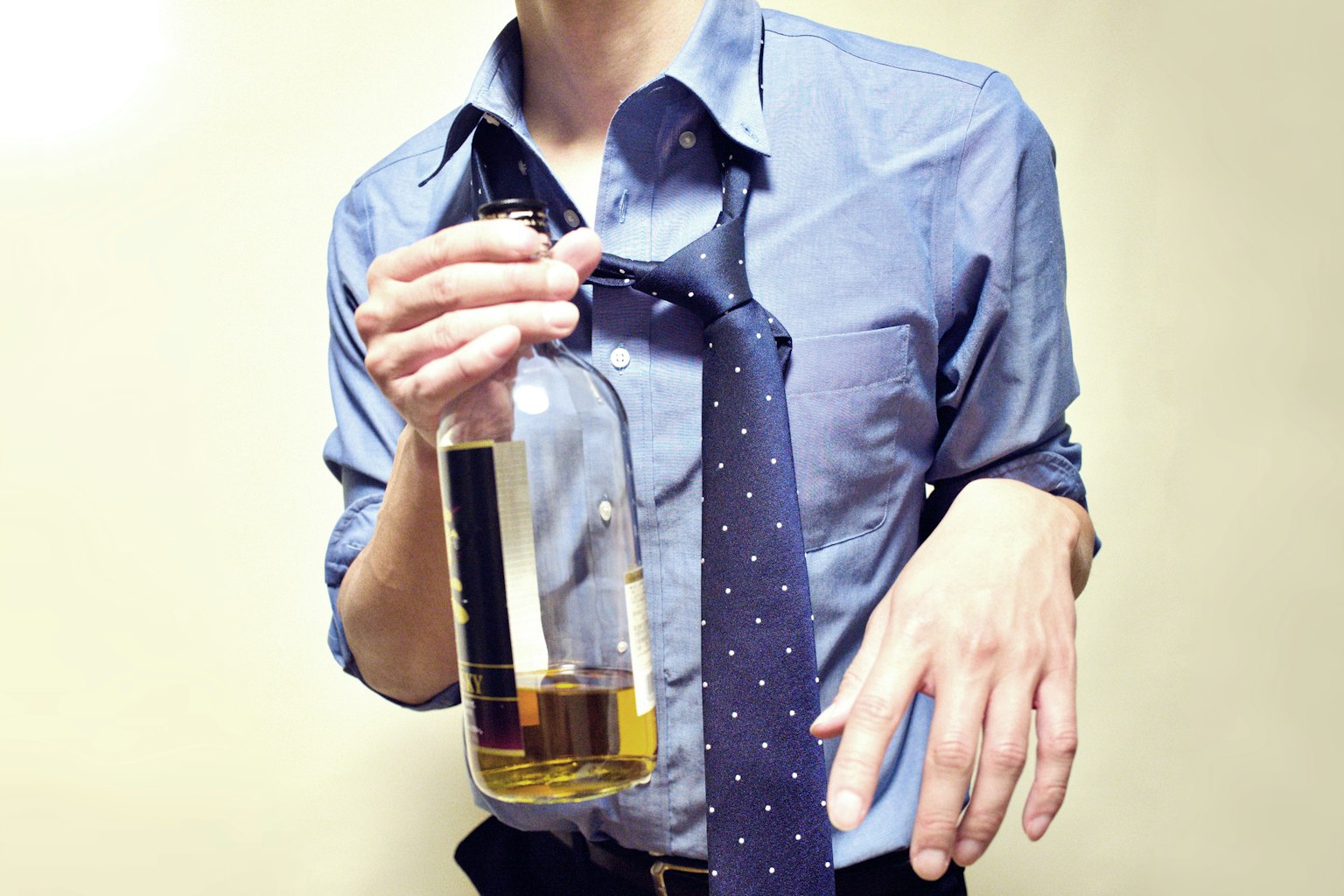 Un uomo in camicia che tiene una bottiglia di liquore con una cravatta allentata attorno al collo