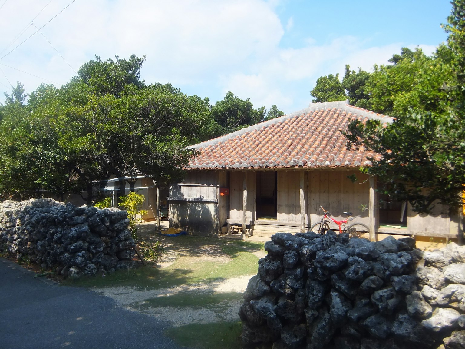 Traditional wooden house with a tiled roof surrounded by stone walls and greenery