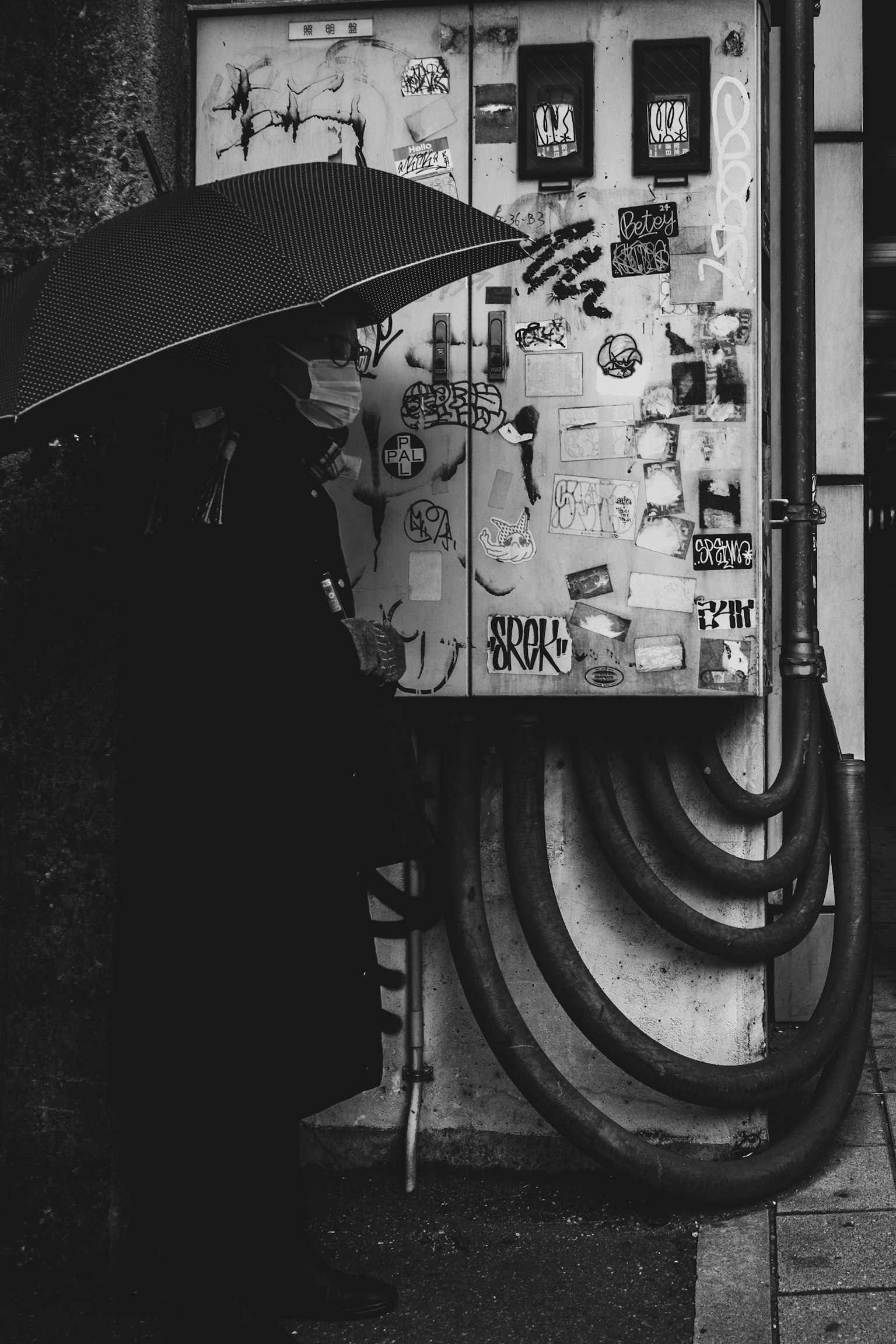 A person holding an umbrella stands in front of a machine covered in stickers