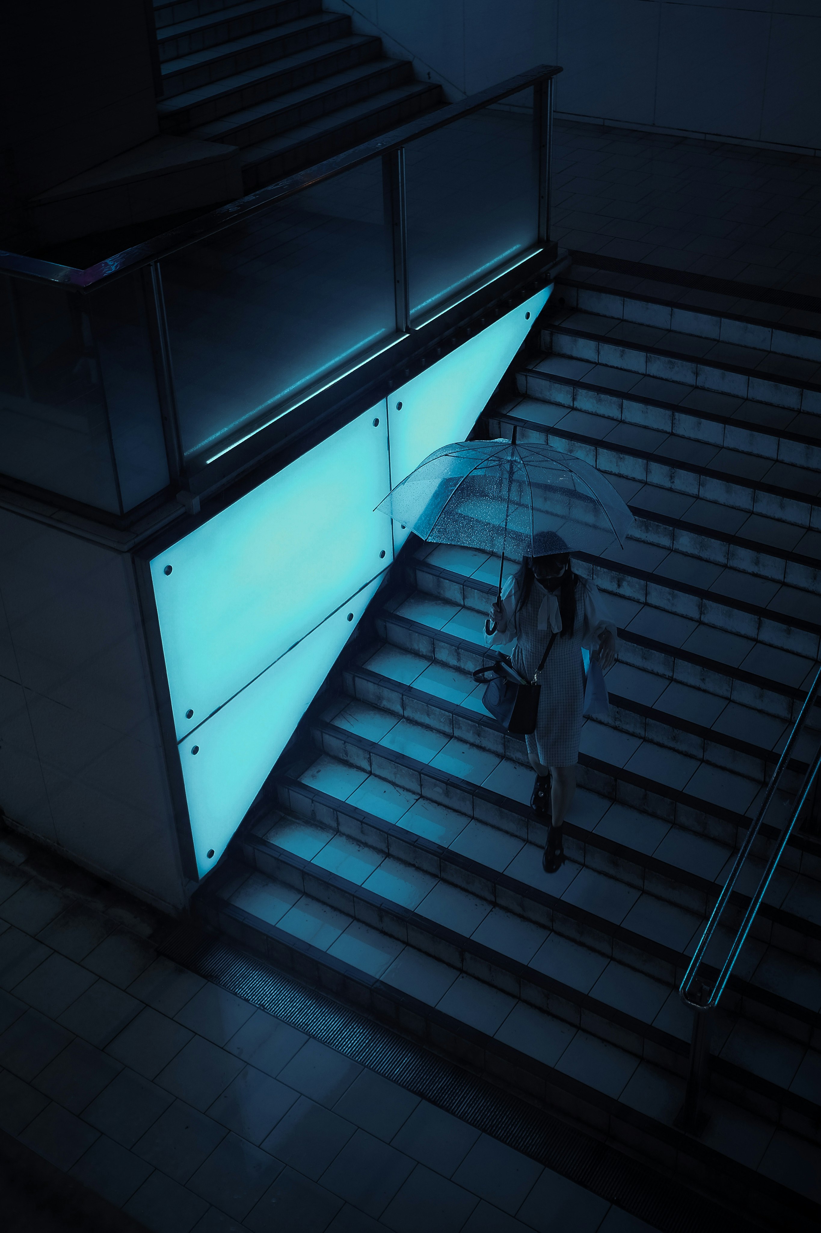 青い光に照らされた階段を降りる人物のシルエット