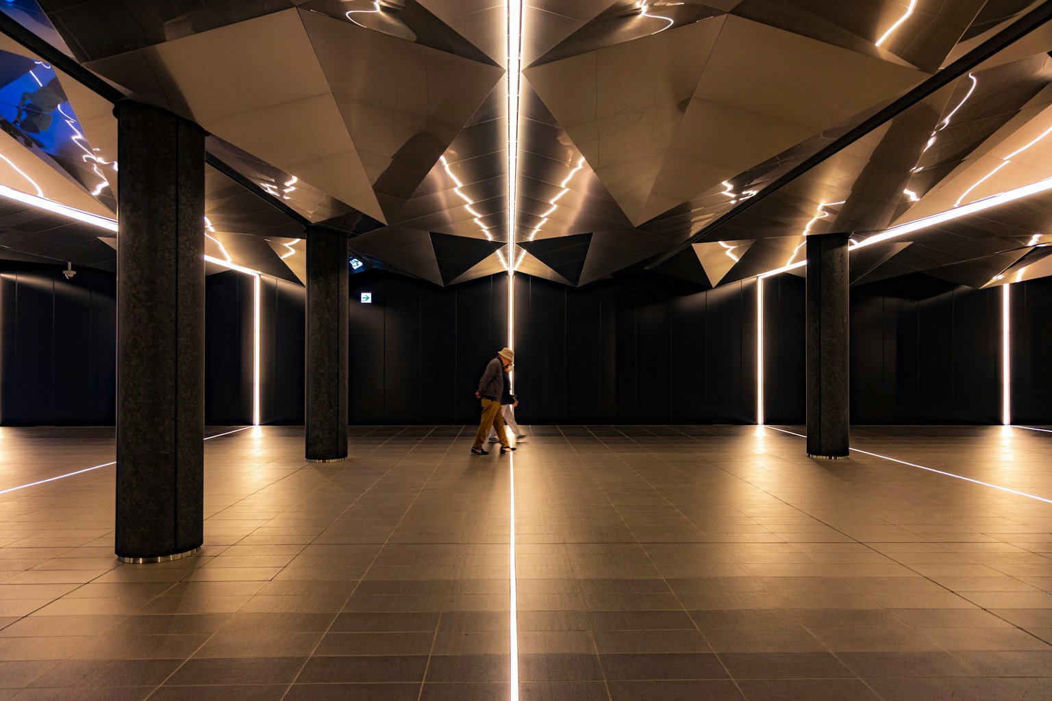 Salle futuriste avec des murs sombres et une ligne lumineuse au sol avec une personne marchant