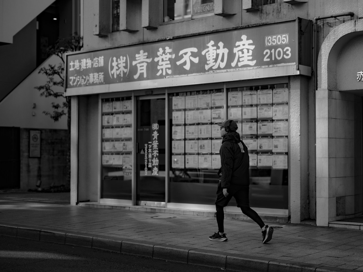 Một người đi bộ trên phố đơn sắc với biển hiệu công ty bất động sản