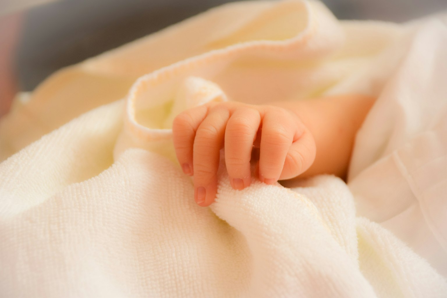 La piccola mano di un bambino che tiene delicatamente una coperta bianca
