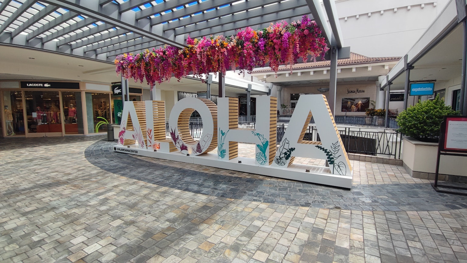 Großes weißes Schild mit ALOHA, dekoriert mit rosa Blumen in einem Einkaufszentrum