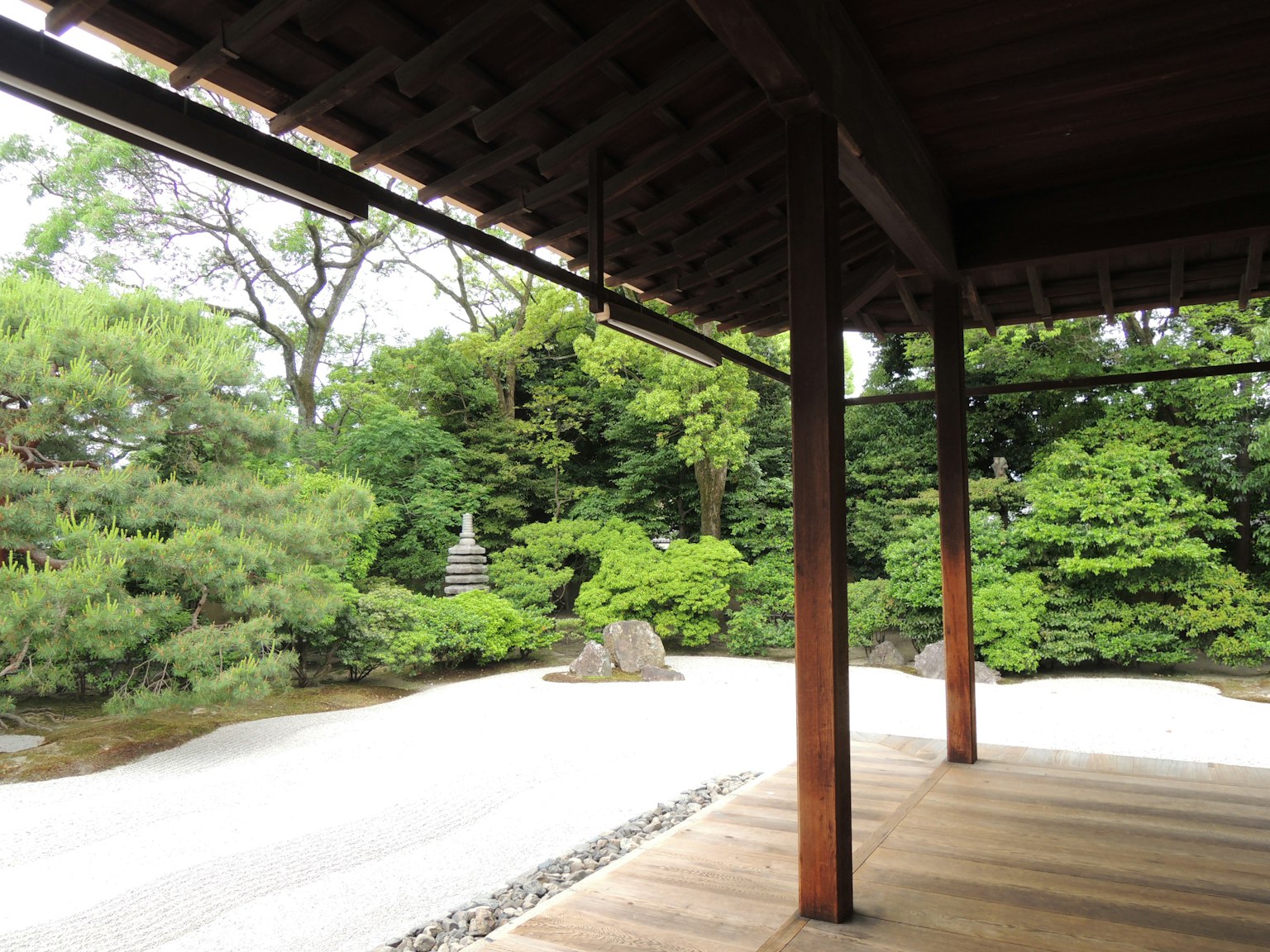 Serene Japanese garden view from a wooden terrace featuring lush greenery and white sand