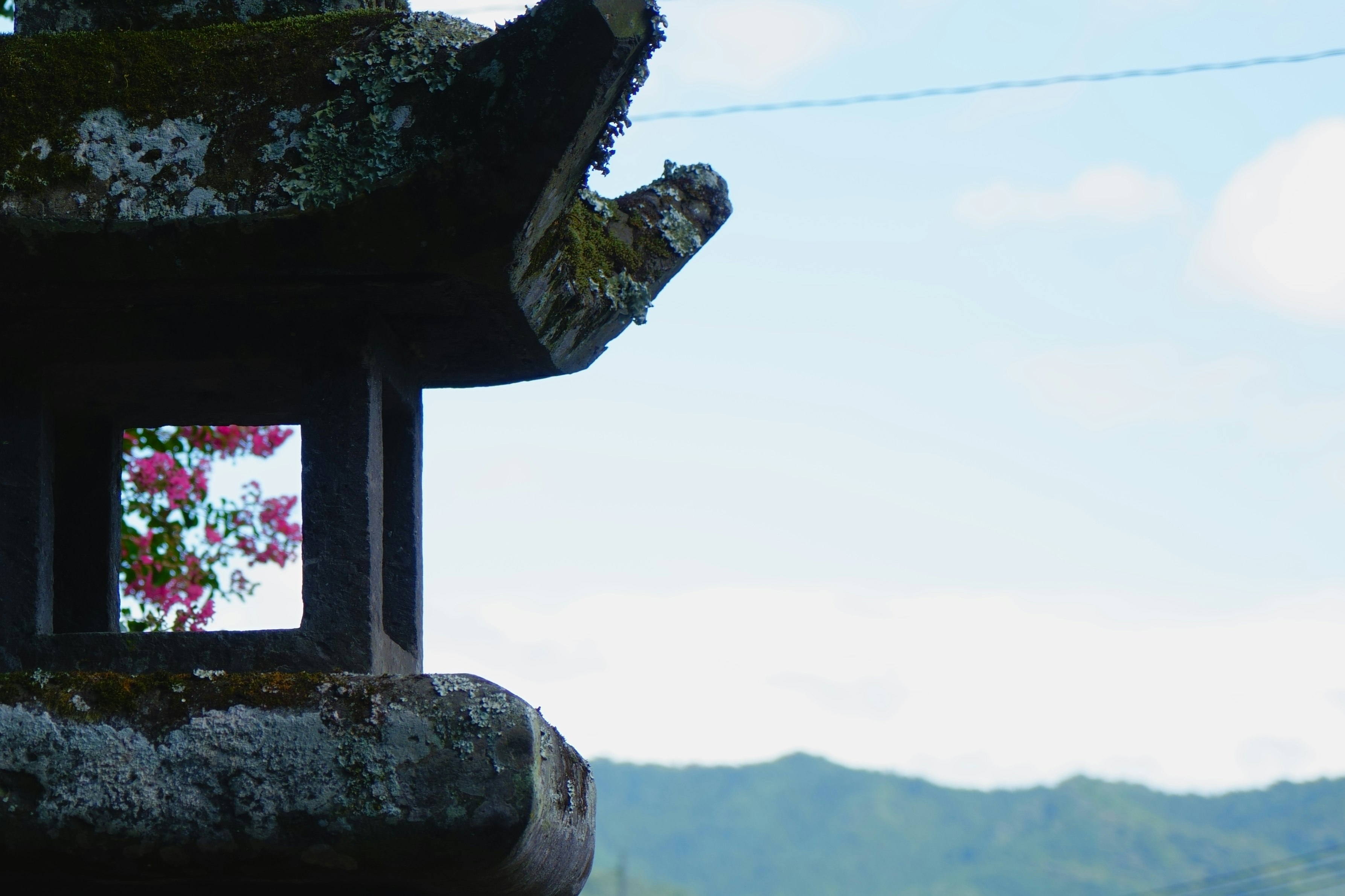 山並みを背景にした灯籠のある寺院の屋根飾り