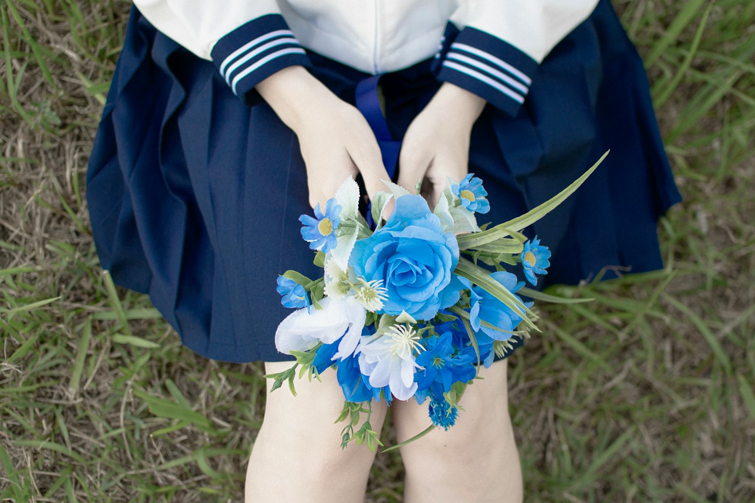 Una ragazza in uniforme che tiene un bouquet blu sulle ginocchia sull'erba