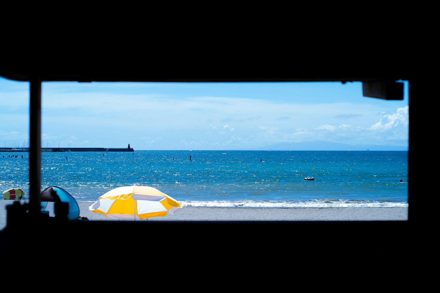 A view of a beach with blue sea and white waves featuring a yellow and white umbrella