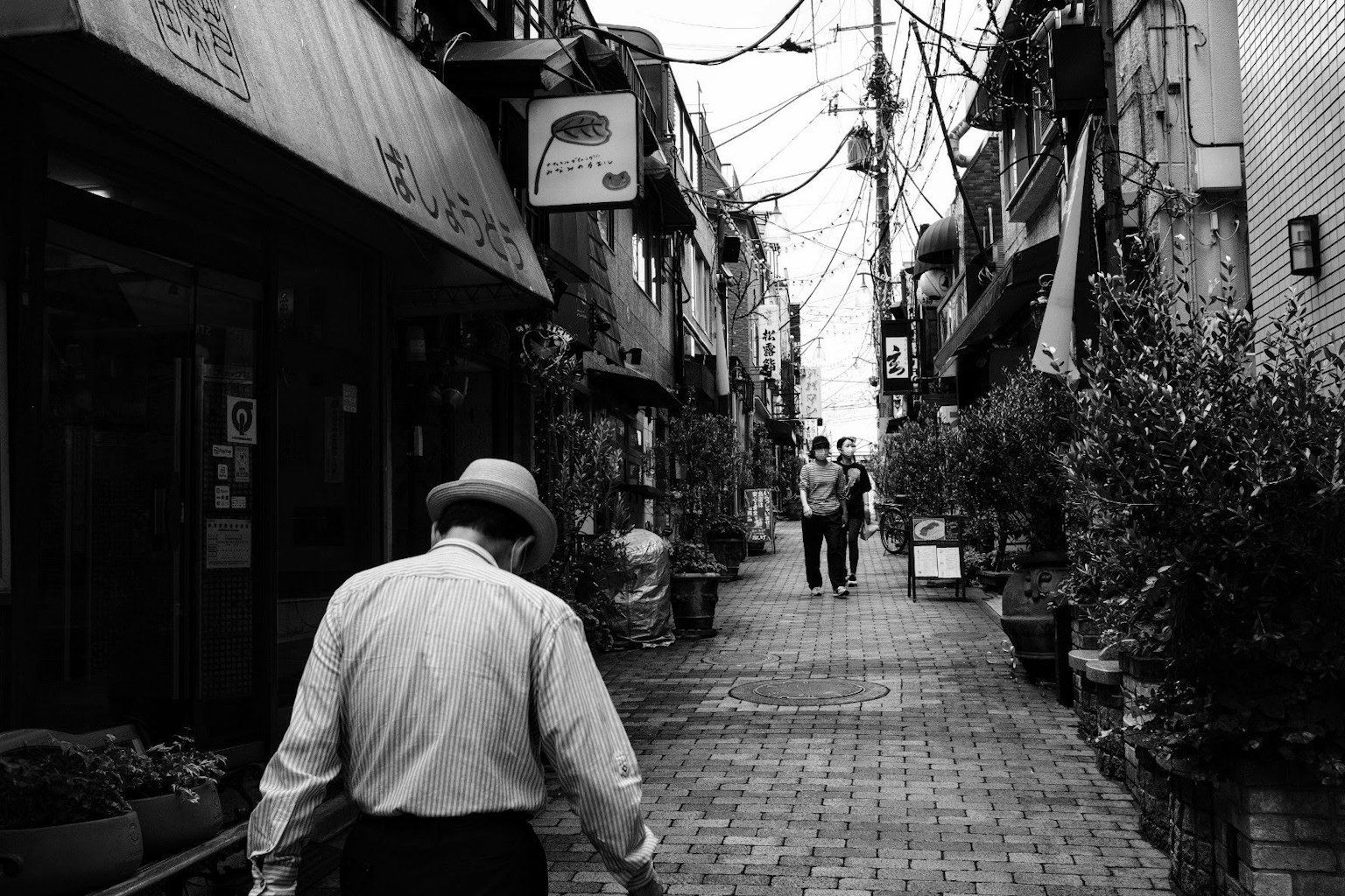 An elderly man walking down a narrow black and white alley with other people