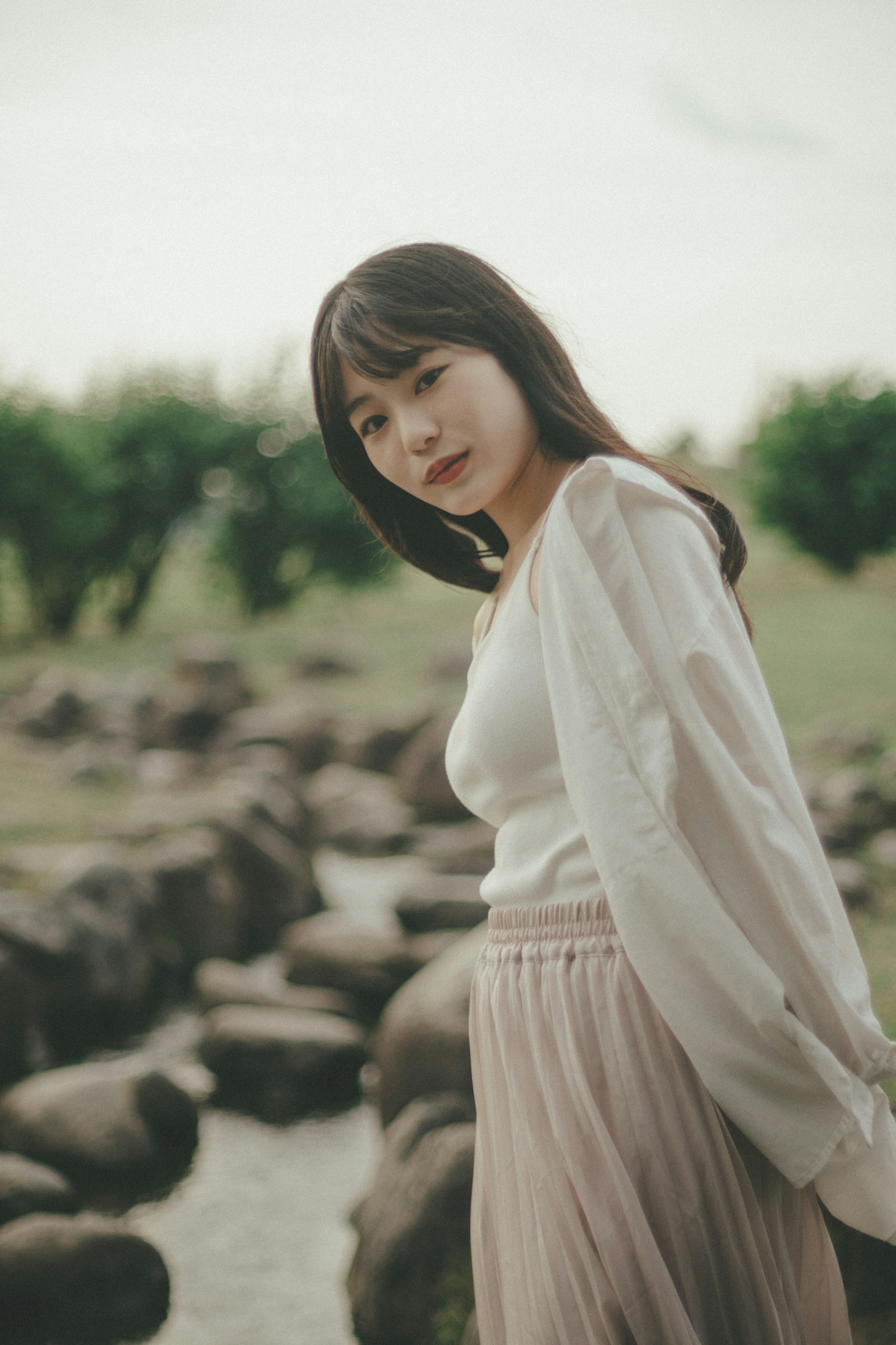 A woman in a light sweater and skirt standing beside a rocky path