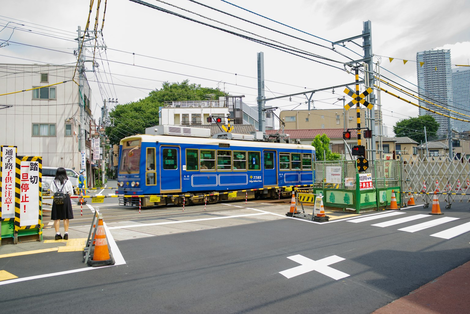 รถรางสีน้ำเงินกำลังผ่านสี่แยก มีการก่อสร้างและสัญญาณจราจรใกล้เคียง