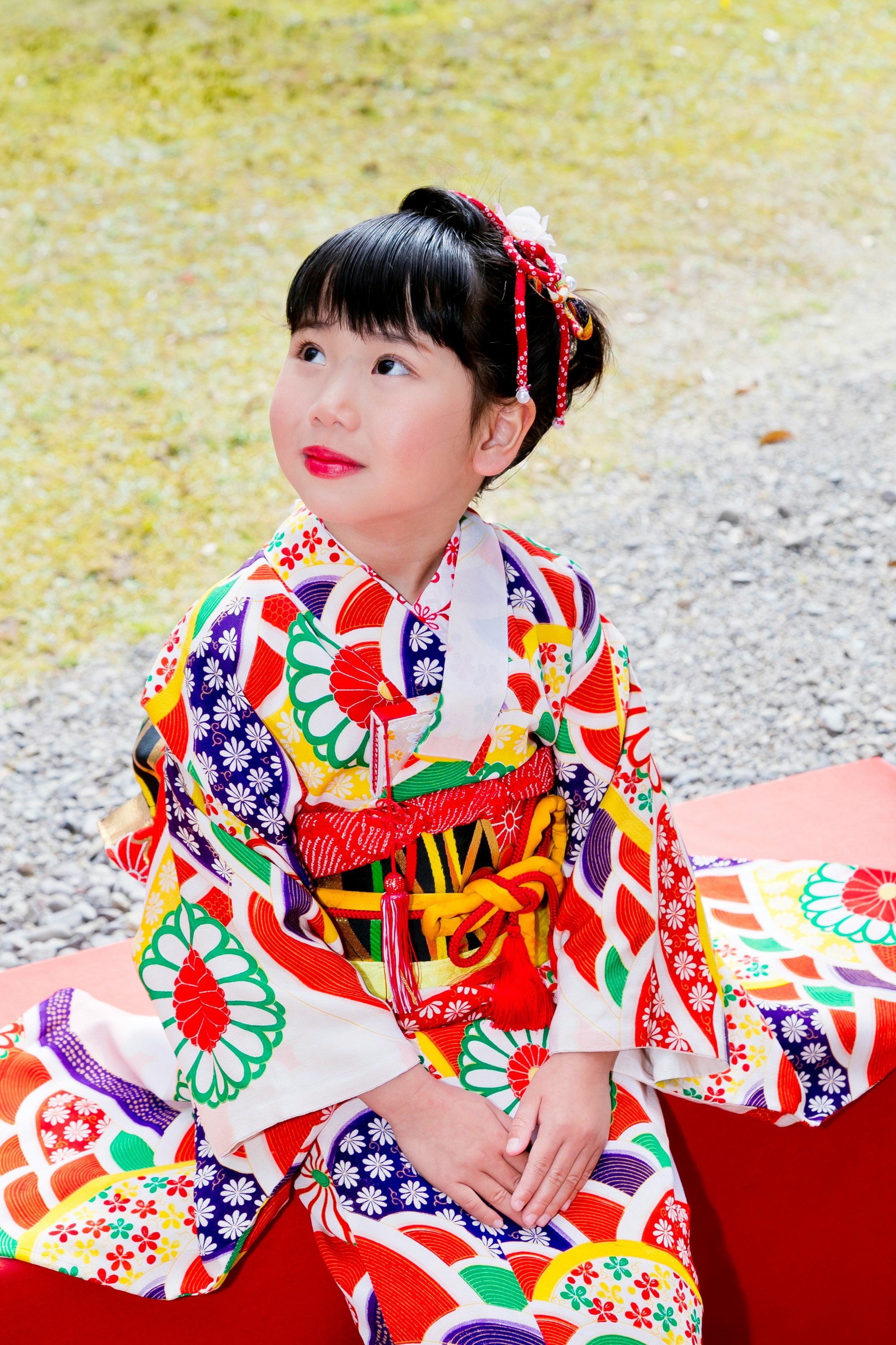Seorang anak memakai kimono berwarna-warni duduk di luar ruangan