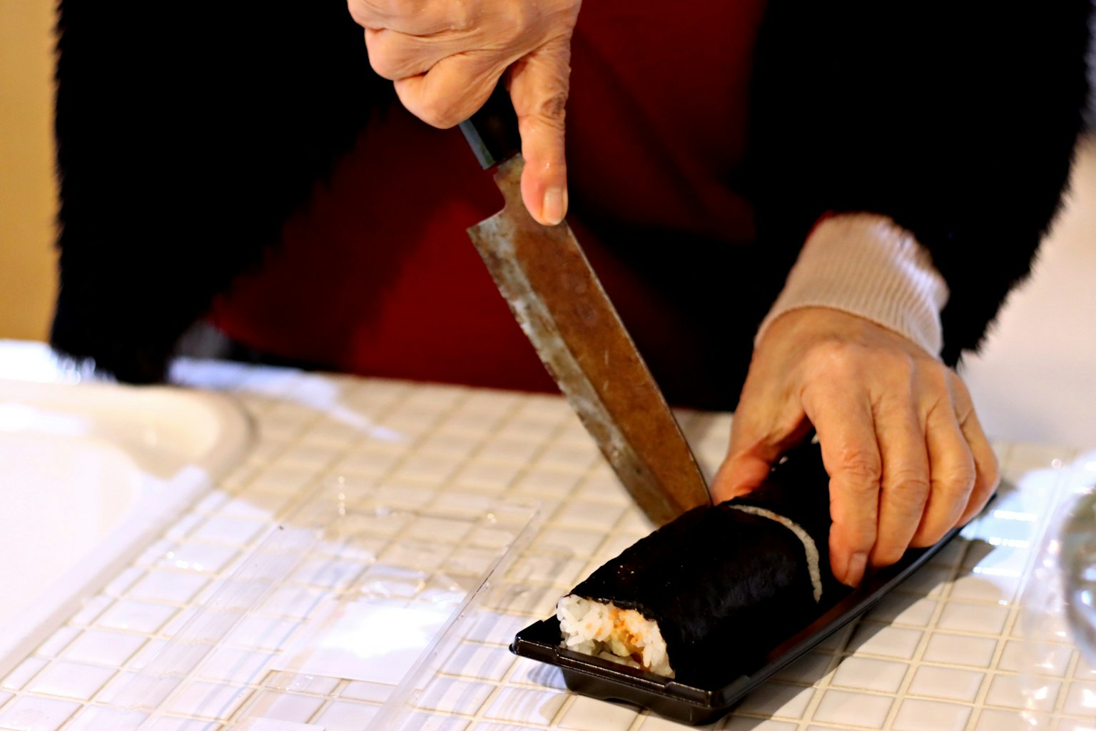 Tangan memotong gulungan sushi dengan pisau di permukaan putih