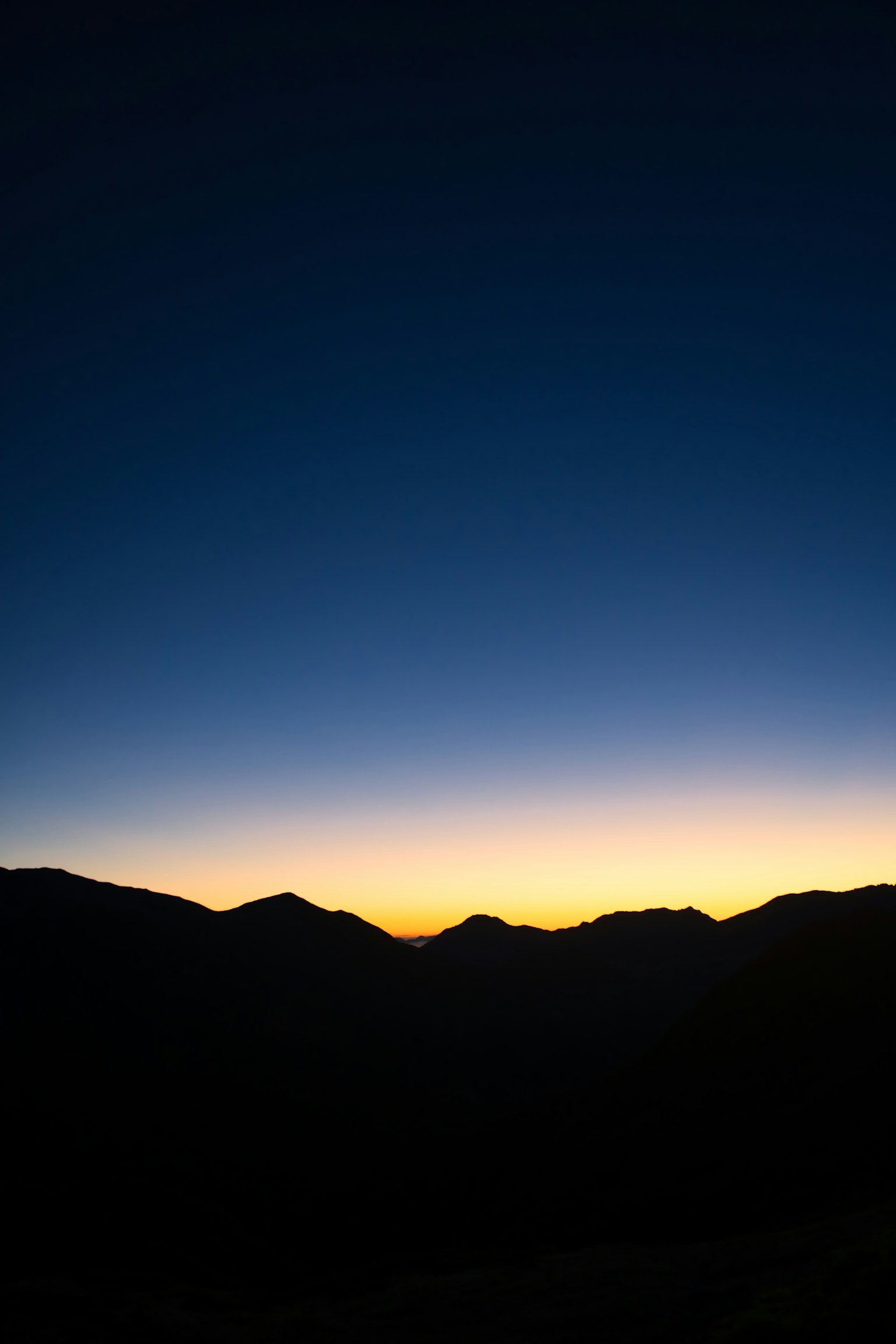 Silhouette von dunklen Bergen vor einem Farbverlaufshimmel von Blau bis Orange