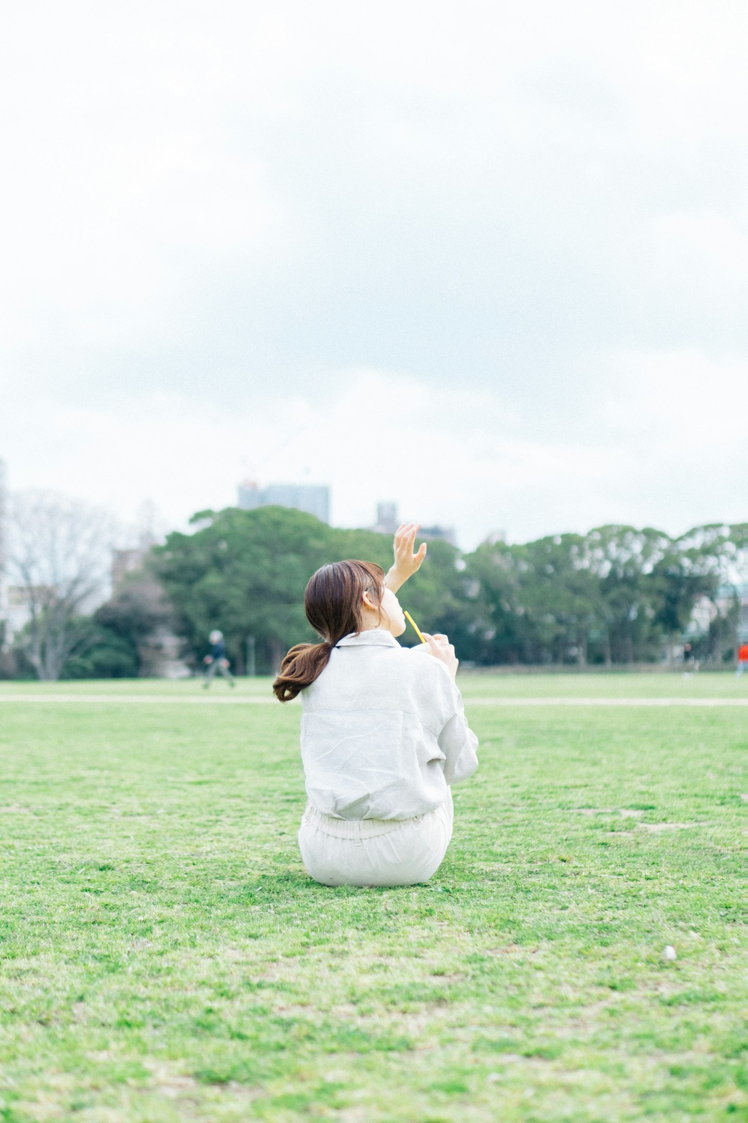 一位女性背對鏡頭坐在公園裡，穿著白色衣服，周圍是綠色草地