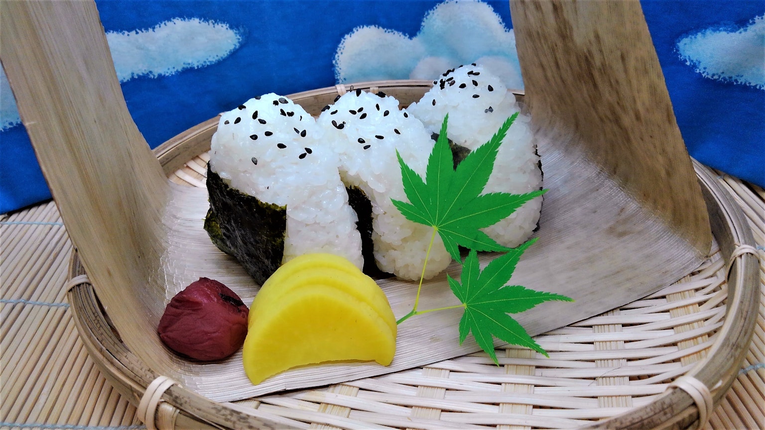 Boules de riz disposées dans un panier en bambou avec des légumes marinés et de l'umeboshi