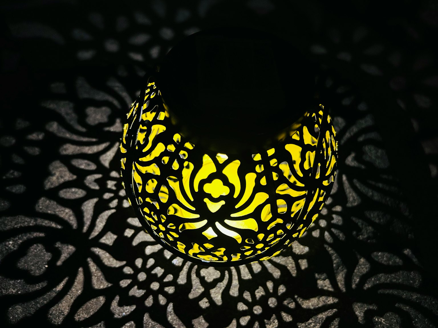 Decorative yellow lamp casting intricate shadows on a dark background