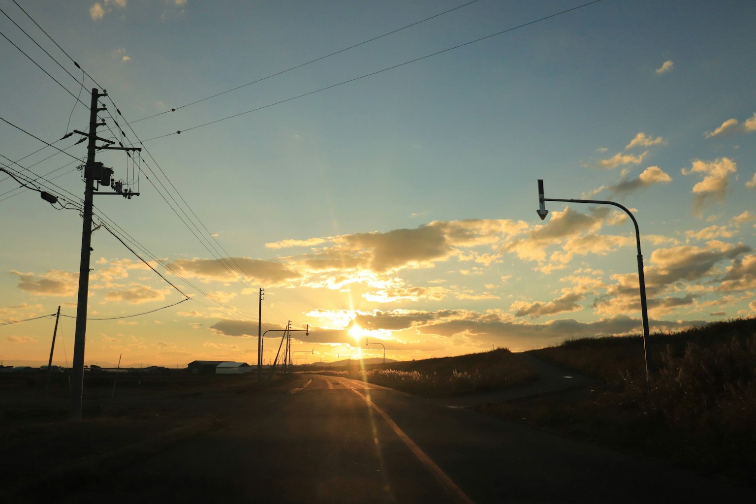 Route illuminée par le ciel au coucher du soleil et lignes électriques