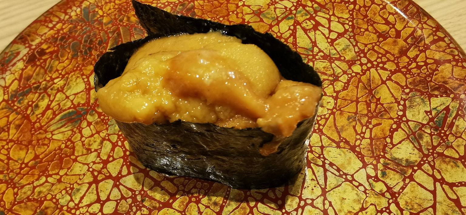 검은 해조류에 싸인 우니 스시가 놓인 장식적인 접시