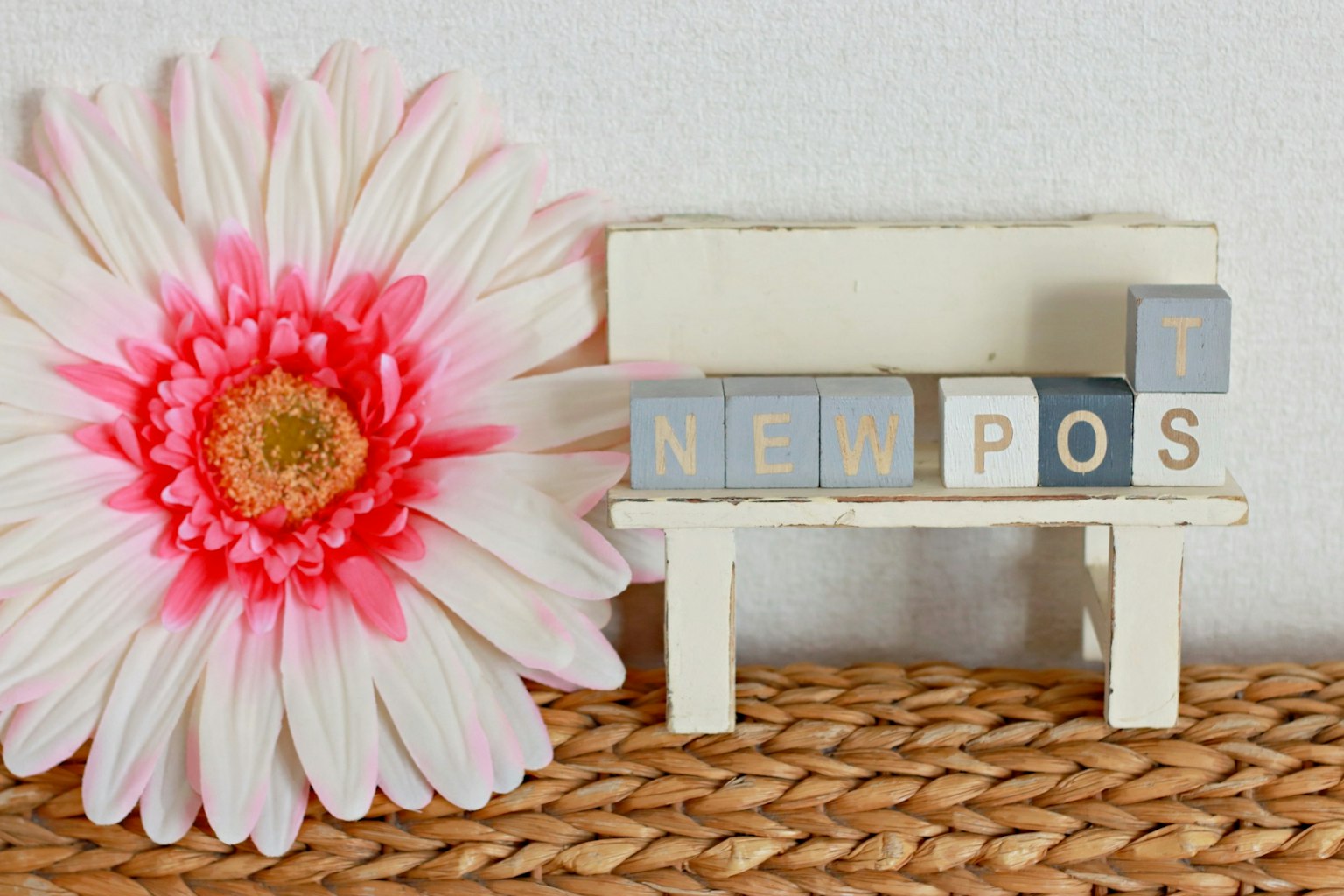 Un pequeño banco blanco con bloques que dicen 'NEW POST' junto a una gran flor rosa