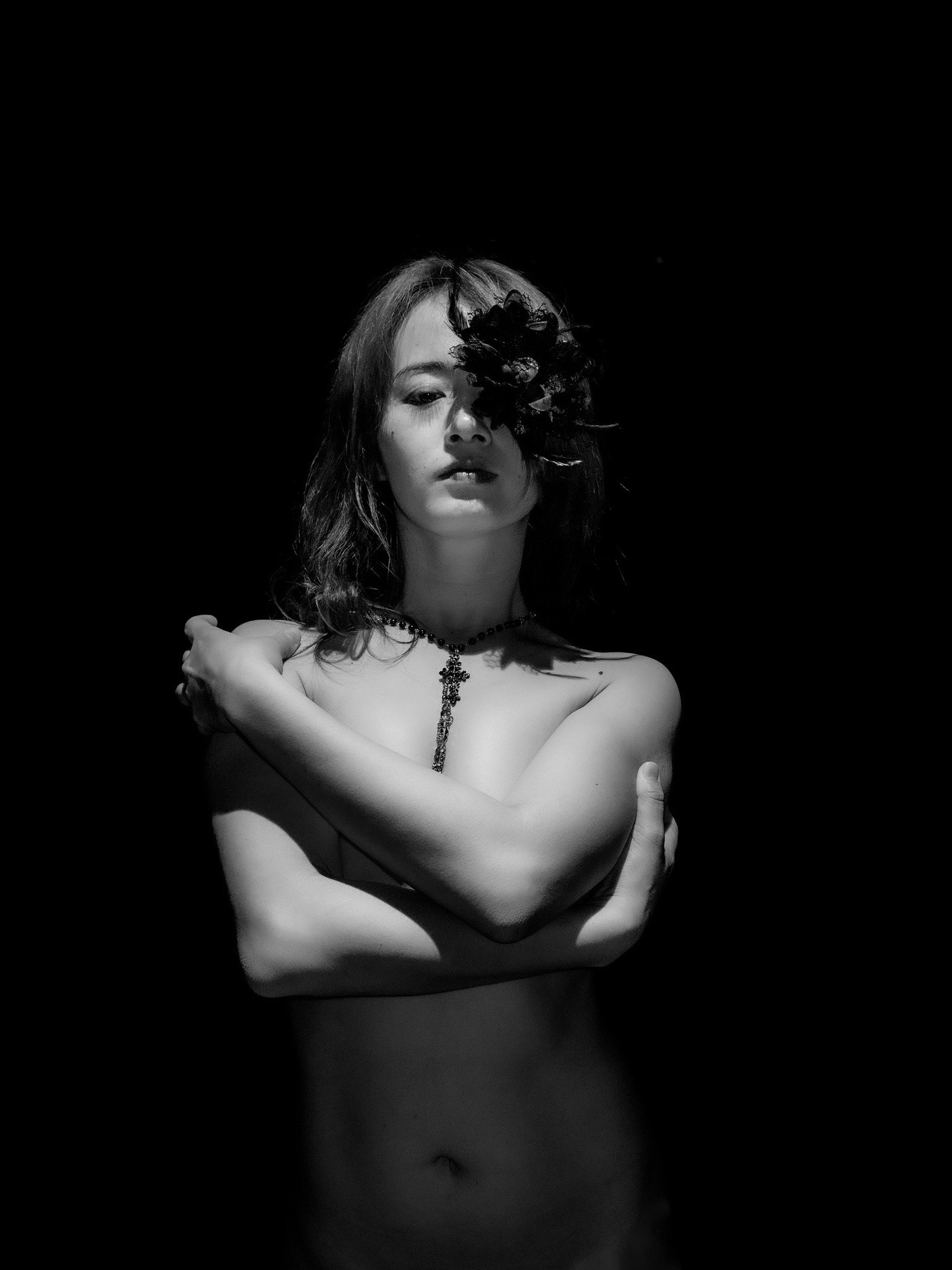黒い背景の前でポーズをとる女性のヌード写真 花が顔の一部を隠している